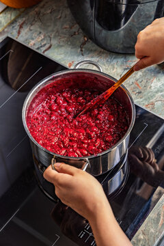 Hands stirring a pot of bubbling cherry jam on a modern induction stovetop