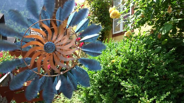 Pinwheel Spinning Kinetic Wind Spinner in Cozy Summer Garden with Roses near House. Windmill weathervane