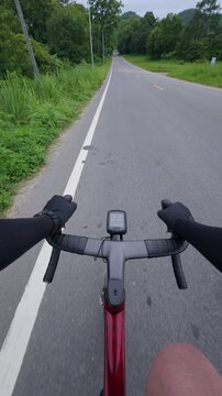 A cyclist's perspective on a rural road, showcasing handlebars and a bike computer amidst lush greenery.
