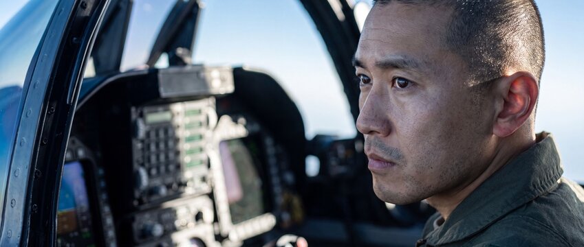 Asian military fighter pilot cockpit flying jet aircraft, serious focused aviator looking ahead during tactical flight mission, air force officer in military aviation defense transport career concept