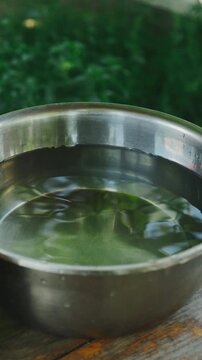 Close view of stainless steel bowl with ripples on weathered wood beside blurred green foliage outdoors