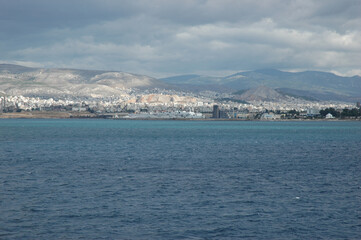 Fototapeta premium Scenic view of Piraeus coastal city and port architecture with mountain landscape under a cloudy sky in Greece