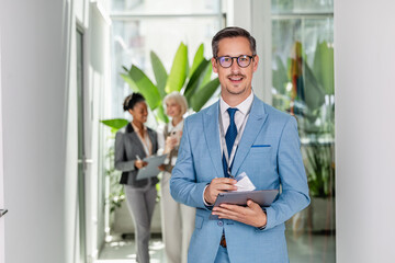 Fototapeta premium Business professional in office lobby holding tablet with colleagues in background