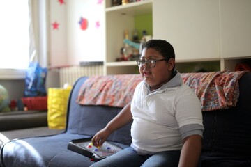 Young boy with glasses plays a game on the couch © Cavan