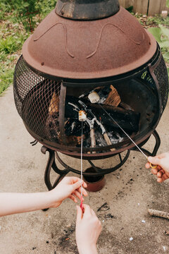 Hands roasting marshmallows over an outdoor fire pit