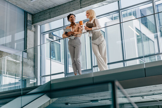 Two business colleagues standing in modern office balcony talking over coffee and documents