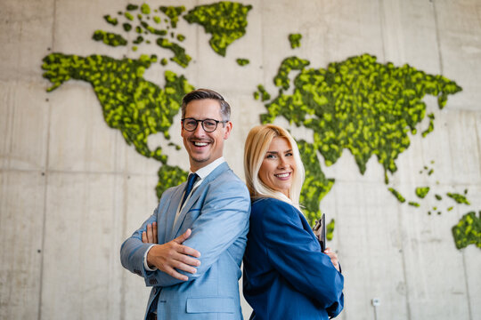 Confident Caucasian European business partners standing back to back in front of green world map