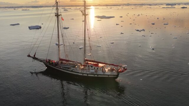 Tall ship sailing through an arctic icefjord at sunset