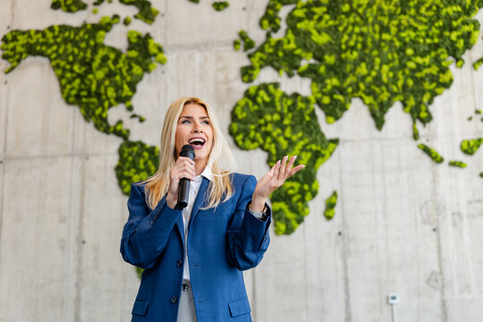 Business speaker presenting sustainable global strategy in front of living world map, Caucasian American woman
