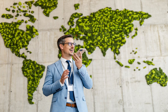 Businessman speaking into smartphone against green world map wall at global conference venue
