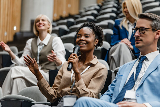 Black businesswoman asking question during corporate conference while colleagues listen and applaud
