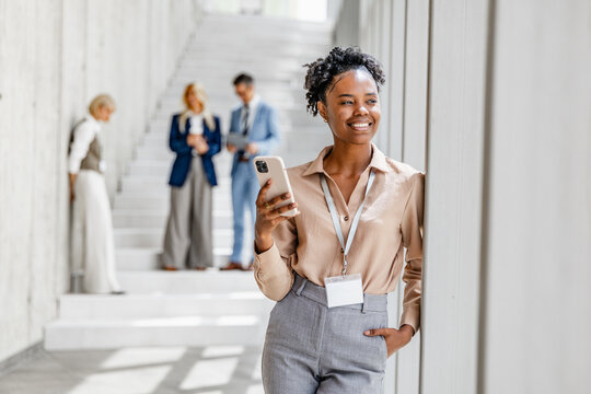 Black professional woman at conference smiling while checking phone in modern stairwell