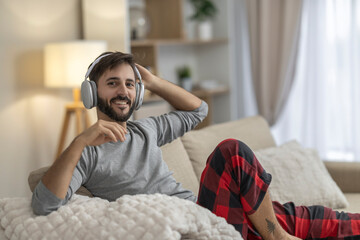 Man relaxing on sofa with headphones smiling in cozy home loungewear