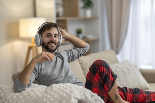 Man relaxing on sofa with headphones smiling in cozy home loungewear