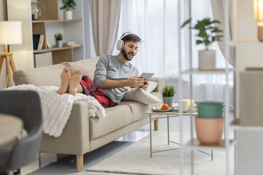 Caucasian man relaxing on sofa with tablet and headphones in modern living room
