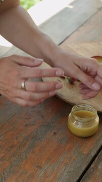 Hands gently open small glass jar of yellow balm beside amber jars on rustic wood in soft warm light hand