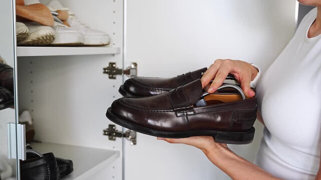 Person placing brown leather loafers into a shoe cabinet. Storage and organization preserve footwear and extend lifespan.