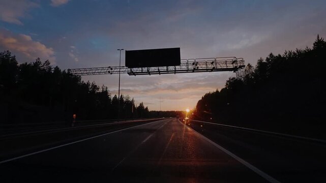 POV perspective driving through a Nordic landscape, where modern highway infrastructure meets dense forests and natural terrain at dusk