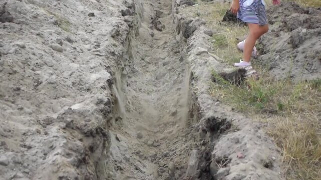 Little girl jumps over an earthen ditch