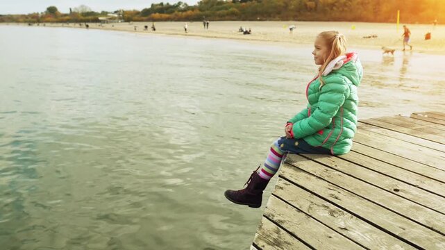 Little beautiful girl sits on wooden pier