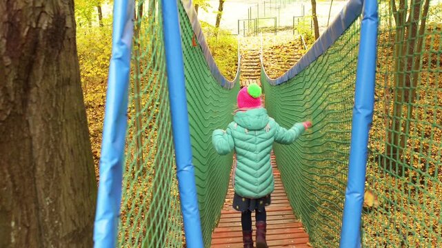 Little girl goes on a long rope bridge in fall park