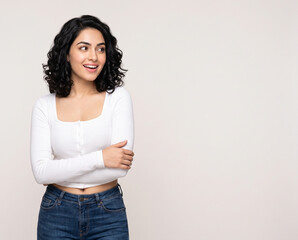 Fototapeta premium Young fair skinned Indian woman looking at copy space with excited smile and relaxed crossed arms for special offer and promotional advertising concept