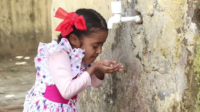 Young Indian thirsty girl child drinking fresh clean water from tap in hot summer. concept of hydration, South Asia water crisis Heat wave, Rural india life.