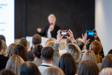 Obraz premium Crowd of attendees record presenter at conference, smartphones held high, focus on audience engagement and live documentation.