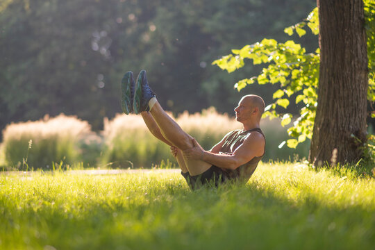 Athletic man practicing boat yoga pose on park grass with copy space