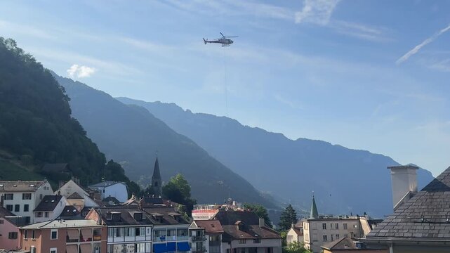 Helicopter Lifting Cargo Over Swiss Alpine Village