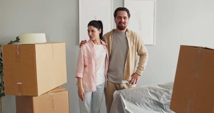 Couple moving home with boxes in new apartment. They stand together as a family, surveying the room, planning layout and envisioning a cozy future. Strong symbol of relocation and teamwork