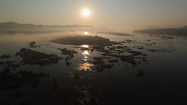 Birds-eye view of beautiful golden sunrise light reflecting on a misty, wide river landscape in Nong Khai Province with exposed boulders
