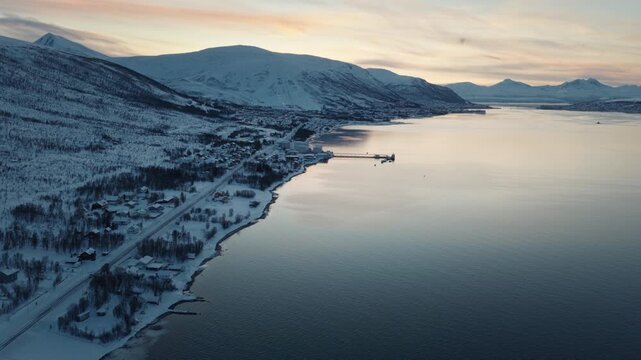 Wide Arctic fjord bordered by snowy mountains beneath pastel skies, drone