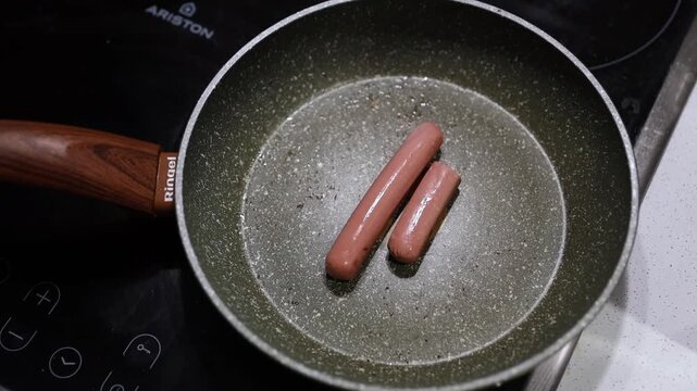 Sausages frying in olive green granite pan on induction cooktop, home cooking concept