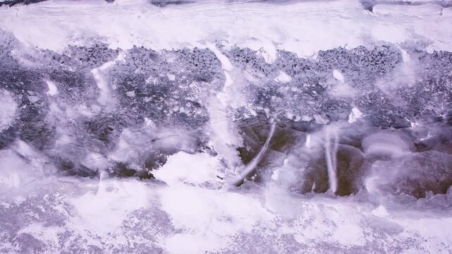 Drone shot looking down at frozen Northern michigan river with interesting patterns of snow and ice