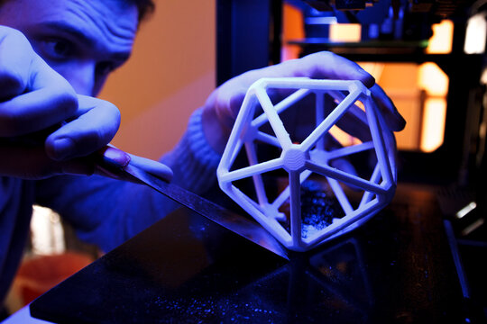 Man using a spatula to separate a 3D geometric figure from the platform of a 3D printer