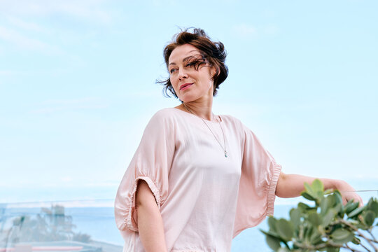 Woman smiling and relaxing by the pool in a pink casual outfit