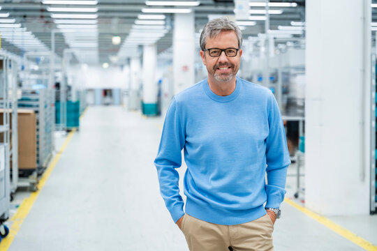 Engineer in production hall smiling with hands in pocket