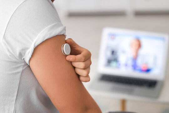 Diabetic young man with glucose sensor receiving online consultation from doctor at home, closeup