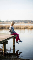 Fototapeta premium Woman on wooden pier looking at calm water, symbolizing reflection, peace, and nature connection, perfect for lifestyle or mental wellness concepts