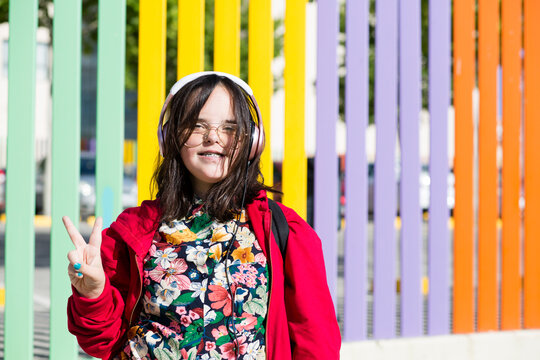 Teenager with down syndrome using smartphone, headphones, peace sign