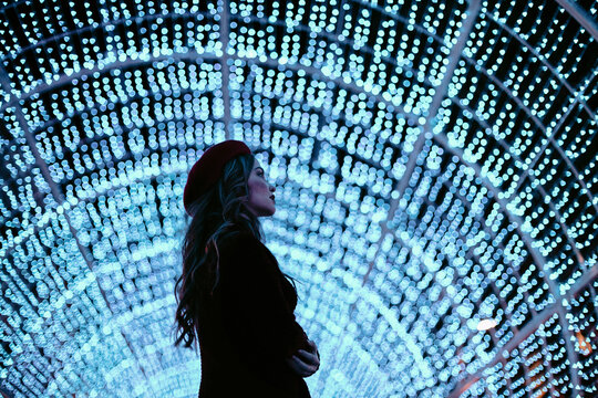 Woman in profile standing in illuminated Christmas light tunnel
