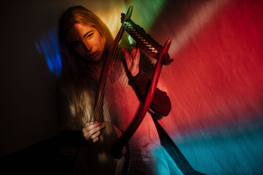 Musician playing a lyre indoors under dramatic colored neon light