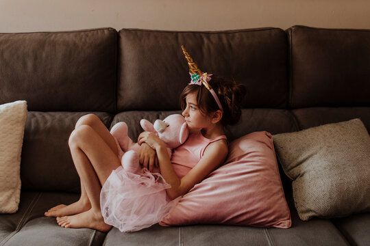 Calm girl wearing unicorn headband resting on sofa with toy