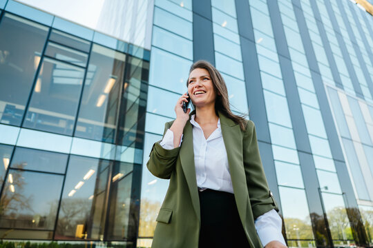 Smiling businesswoman talking on smartphone outside office building