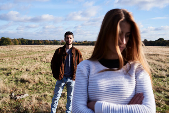 Serious young woman standing on a field with man behind her