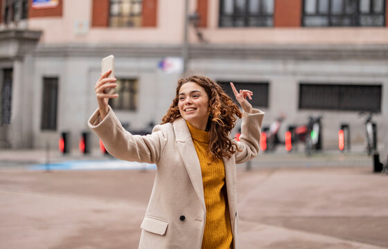 Happy young woman talking on video call and gesturing in front of building