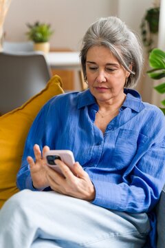 Woman using a smartphone while relaxing on the sofa at home