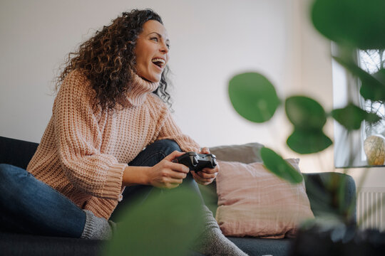 Woman sitting on couch, having fun, playing with a gaming console