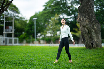 Fototapeta premium Young Woman Walking Barefoot on Green Grass in Park for Grounding and Earthing Wellness Practice